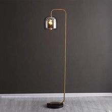 Load image into Gallery viewer, Pitalito floor lamp in situ in living room, amber glass shade casting warm glow
